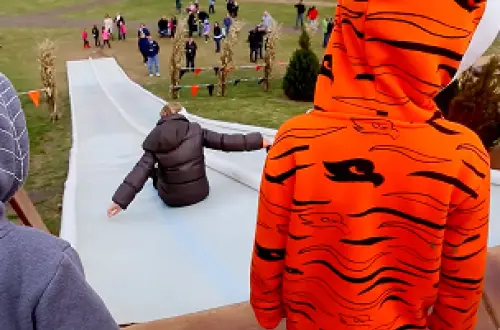 Ein Kind in einem orange-schwarzen Kapuzenpulli wartet darauf, die Rutsche hinunterzurutschen. 