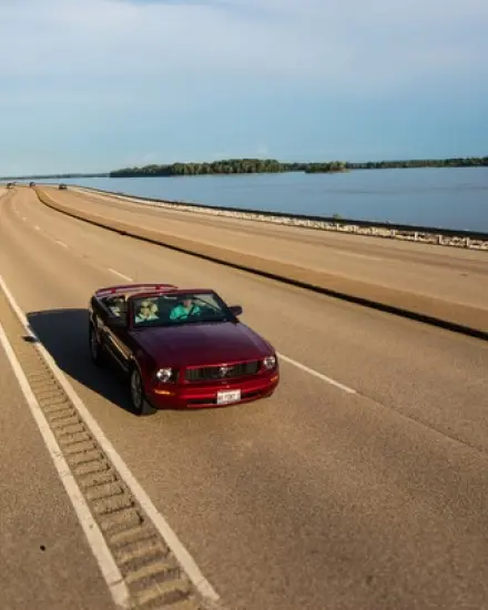 Ein rotes Cabrio, das auf einer malerischen Straße am Mississippi entlangfährt.